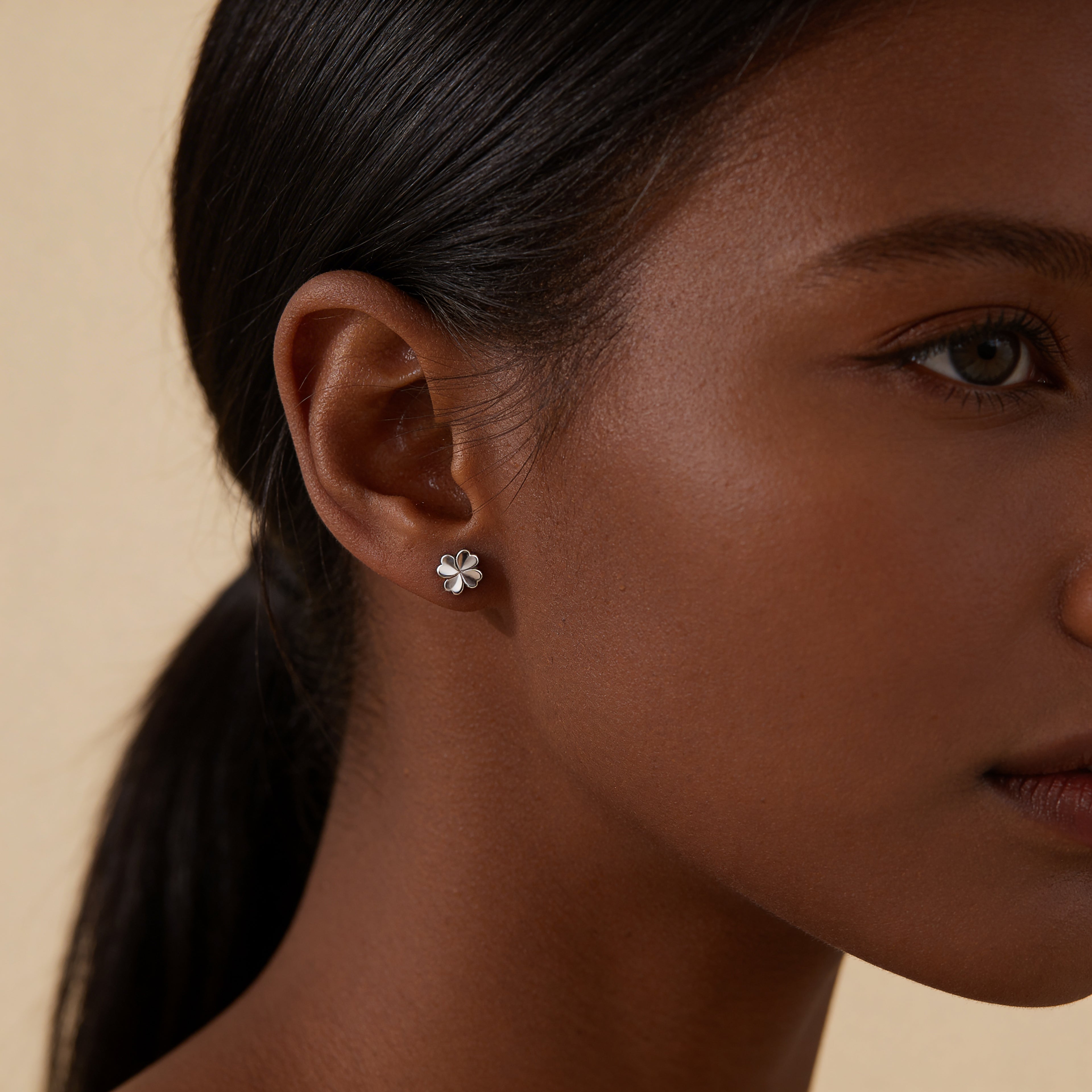 Small silver clover stud earrings worn on ear.
