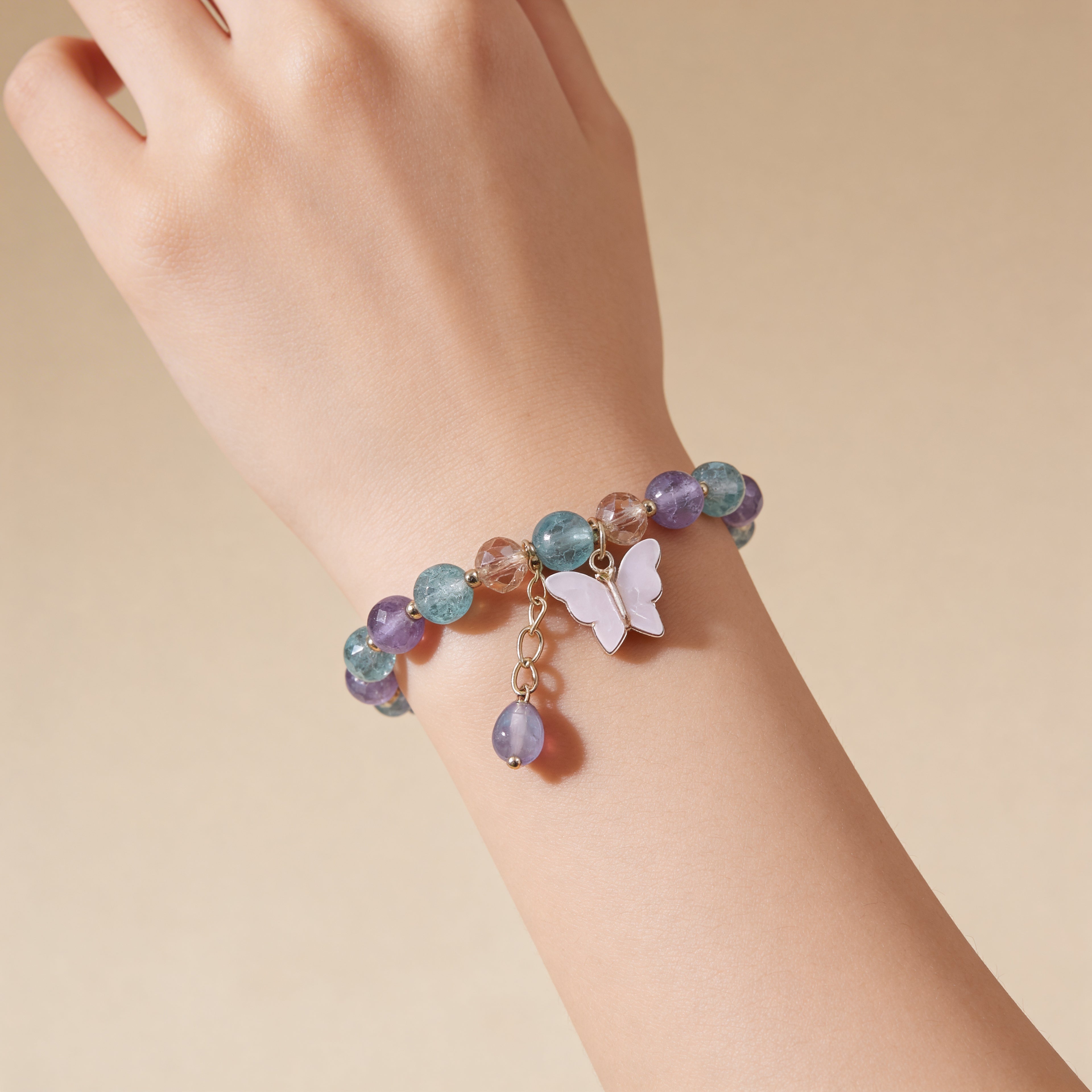 Pink beaded bracelet with a butterfly charm on a white background