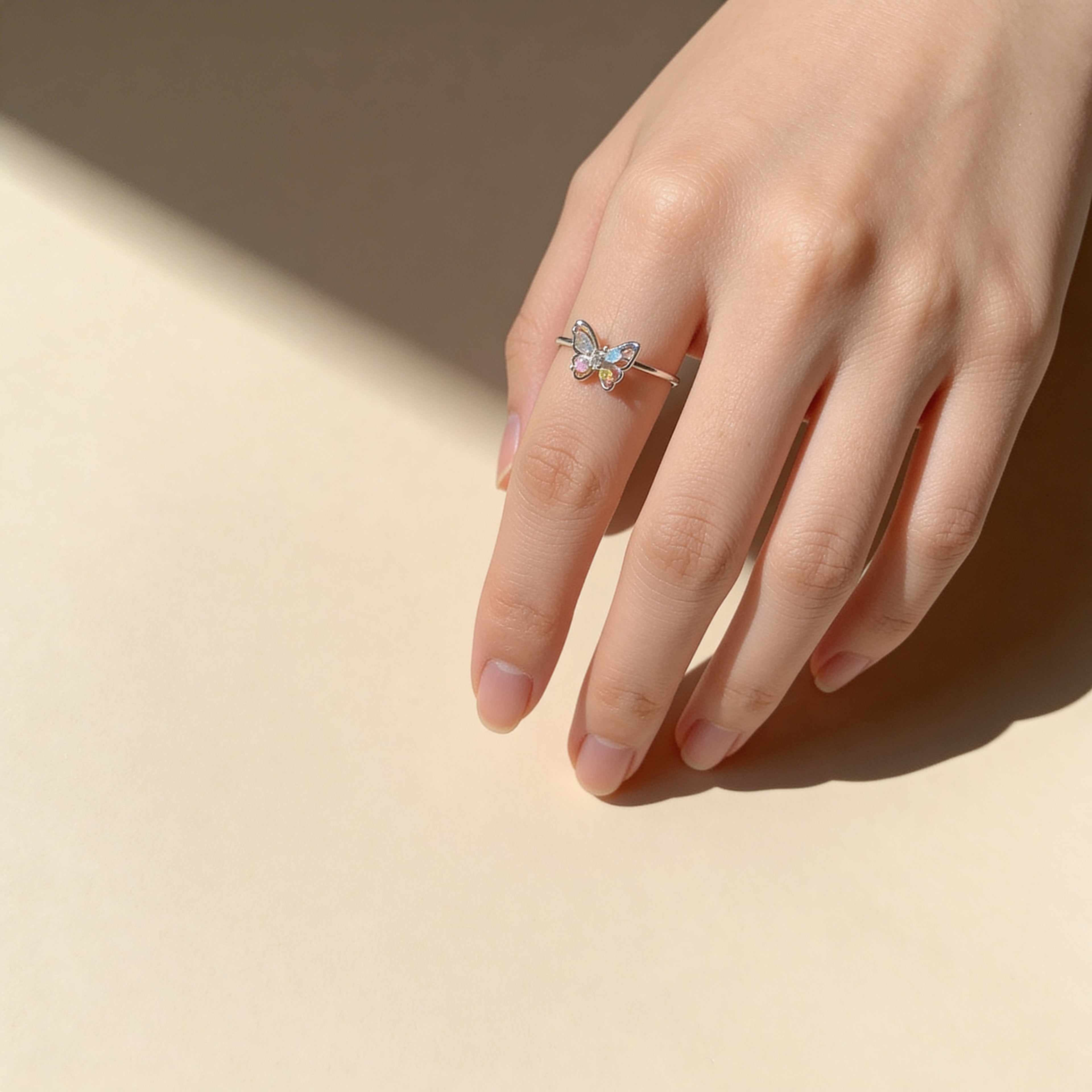 Dainty silver butterfly ring with multicolor stones styled on hand.