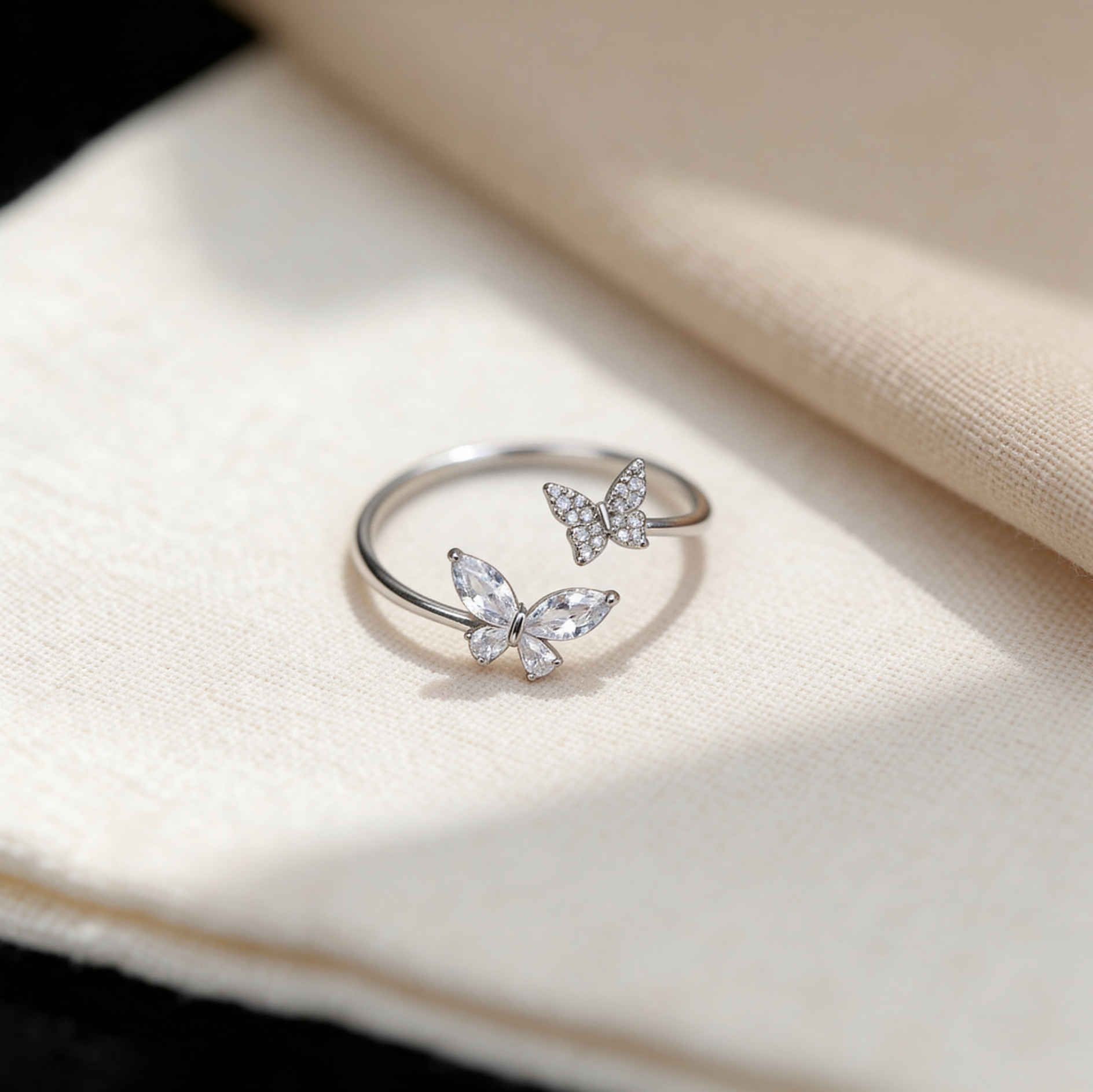 Adjustable silver plated double butterfly ring with sparkling cubic zirconia crystals displayed on beige fabric