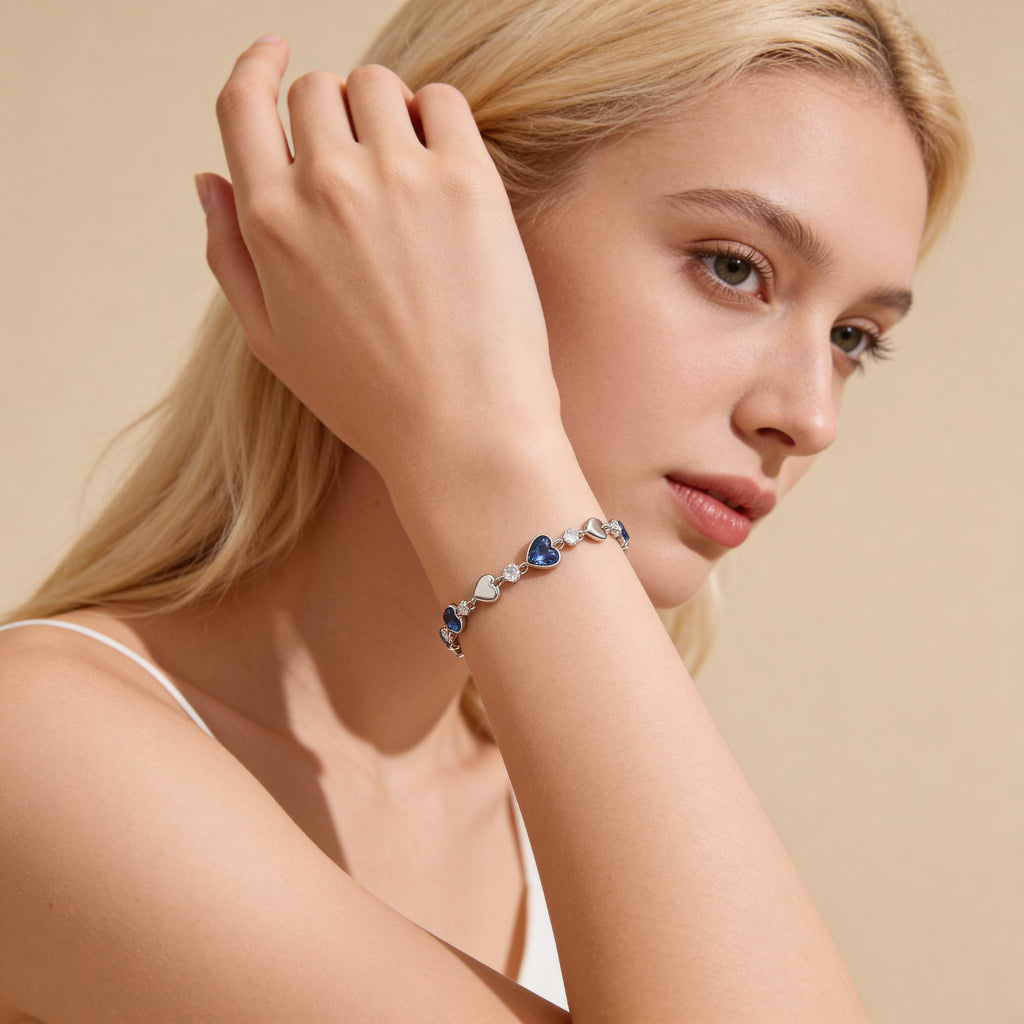 Dainty silver blue heart charm bracelet worn on wrist.