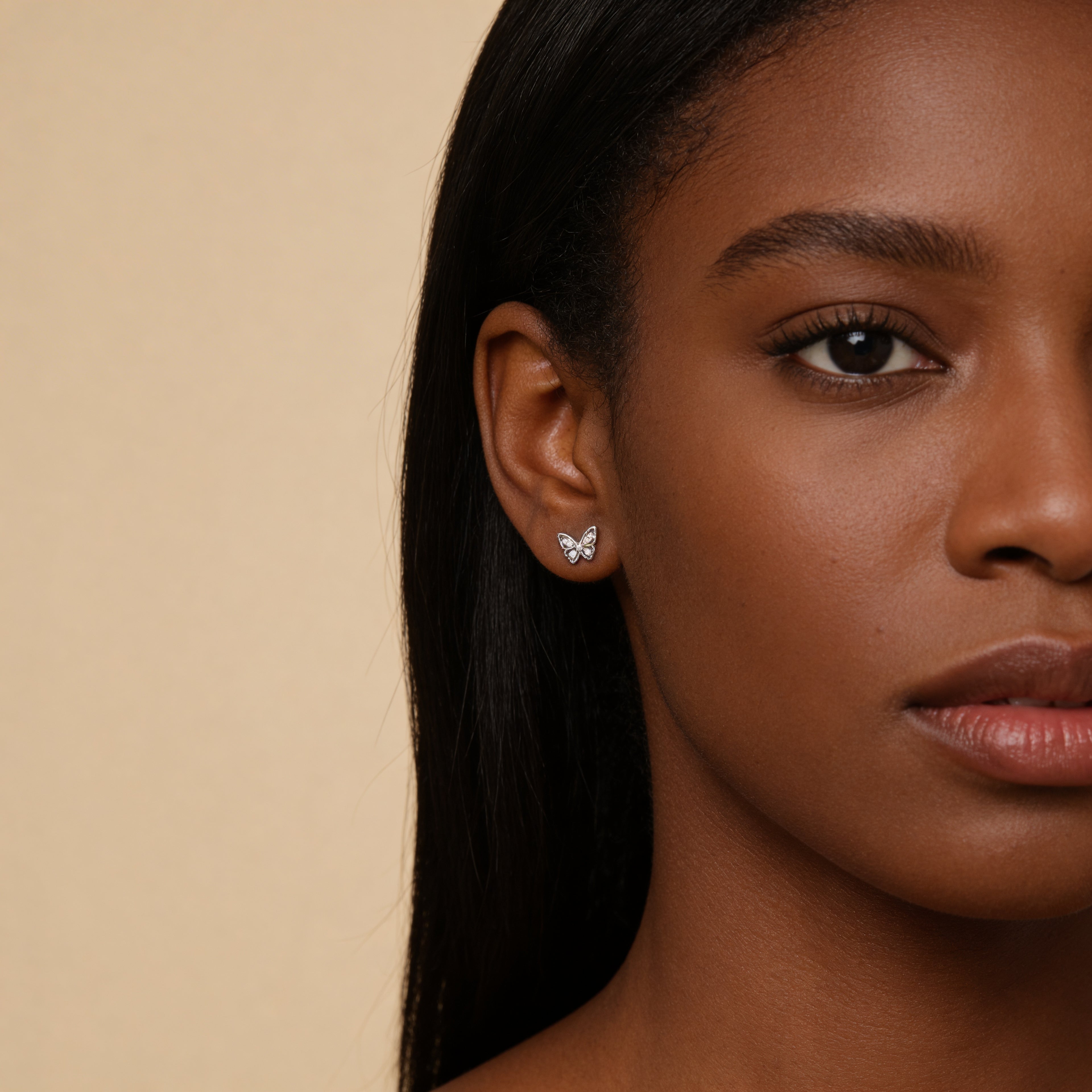 Close-up of a woman wearing butterfly earrings with a beige background
