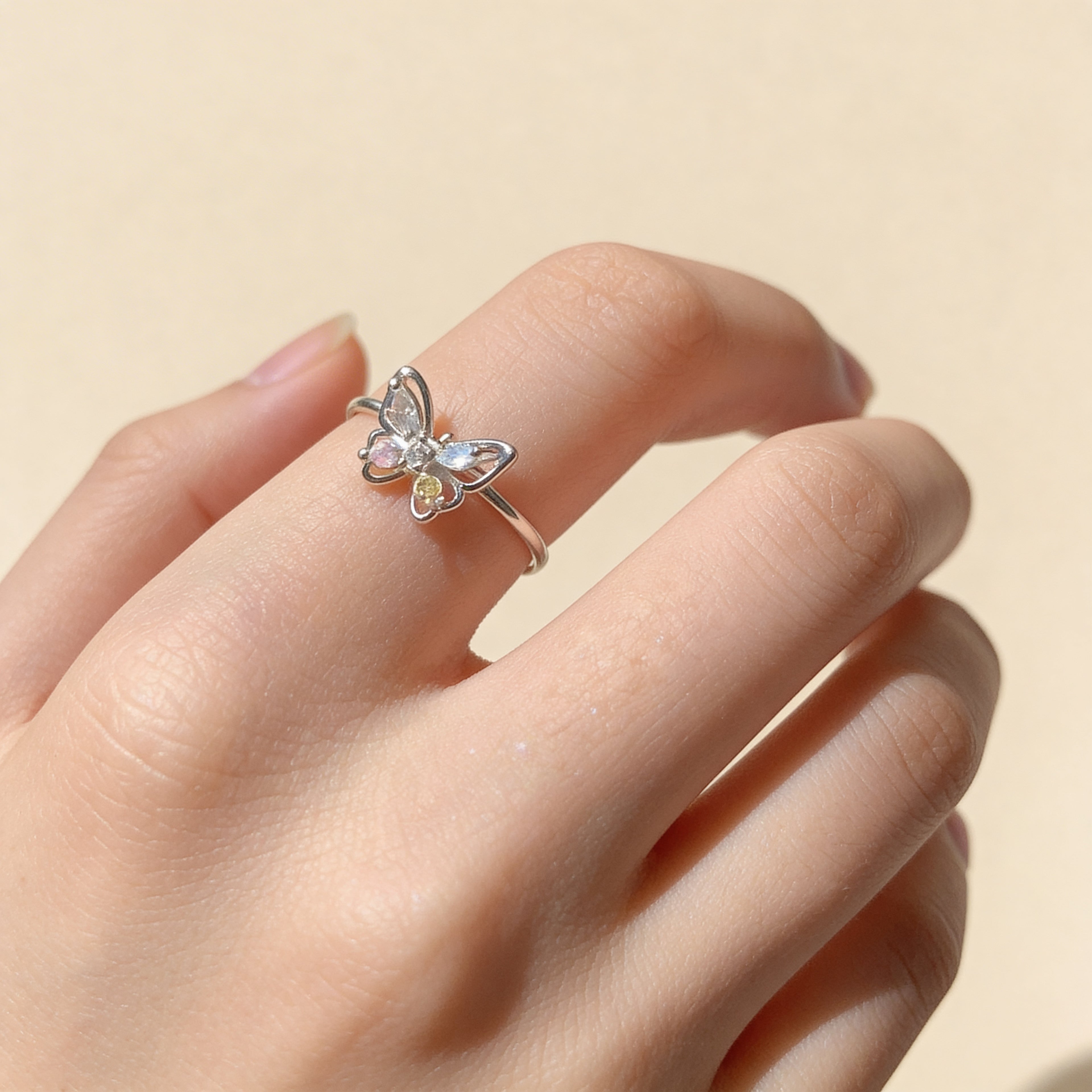 Adjustable silver butterfly ring worn on finger with colorful crystal details.