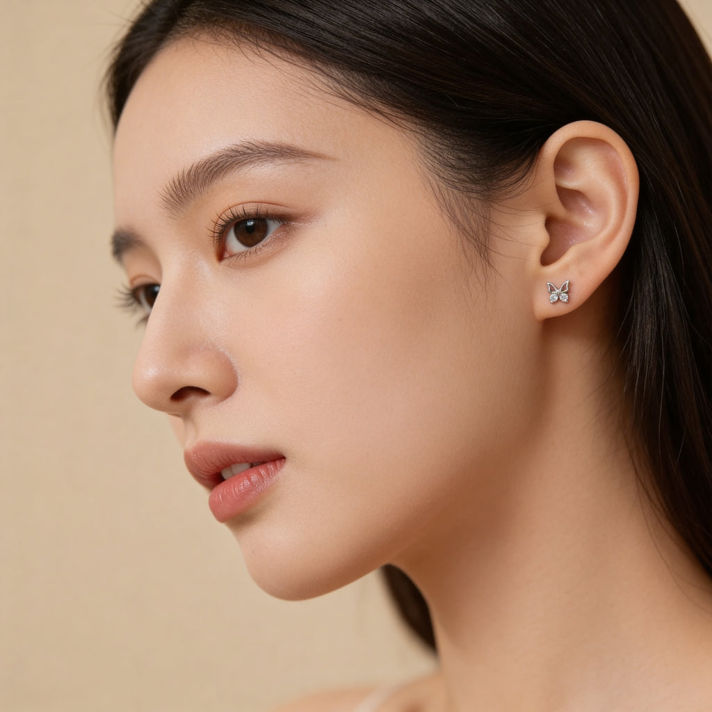 Small silver butterfly stud earrings worn on ear.