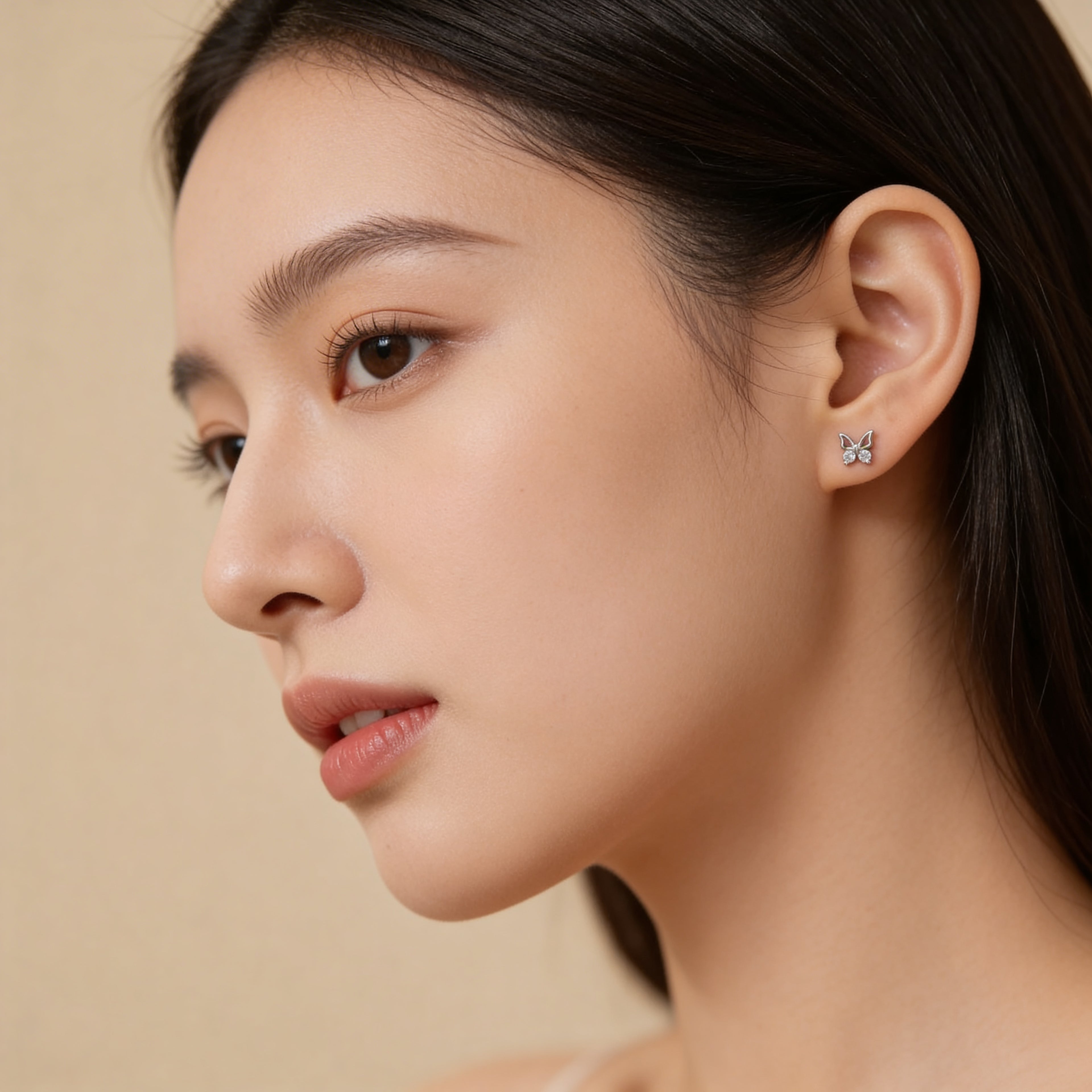 Small silver butterfly stud earrings worn on ear.
