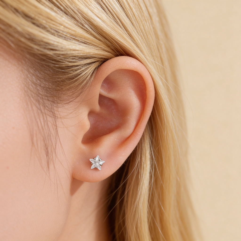 Tiny crystal star stud earrings worn on ear.