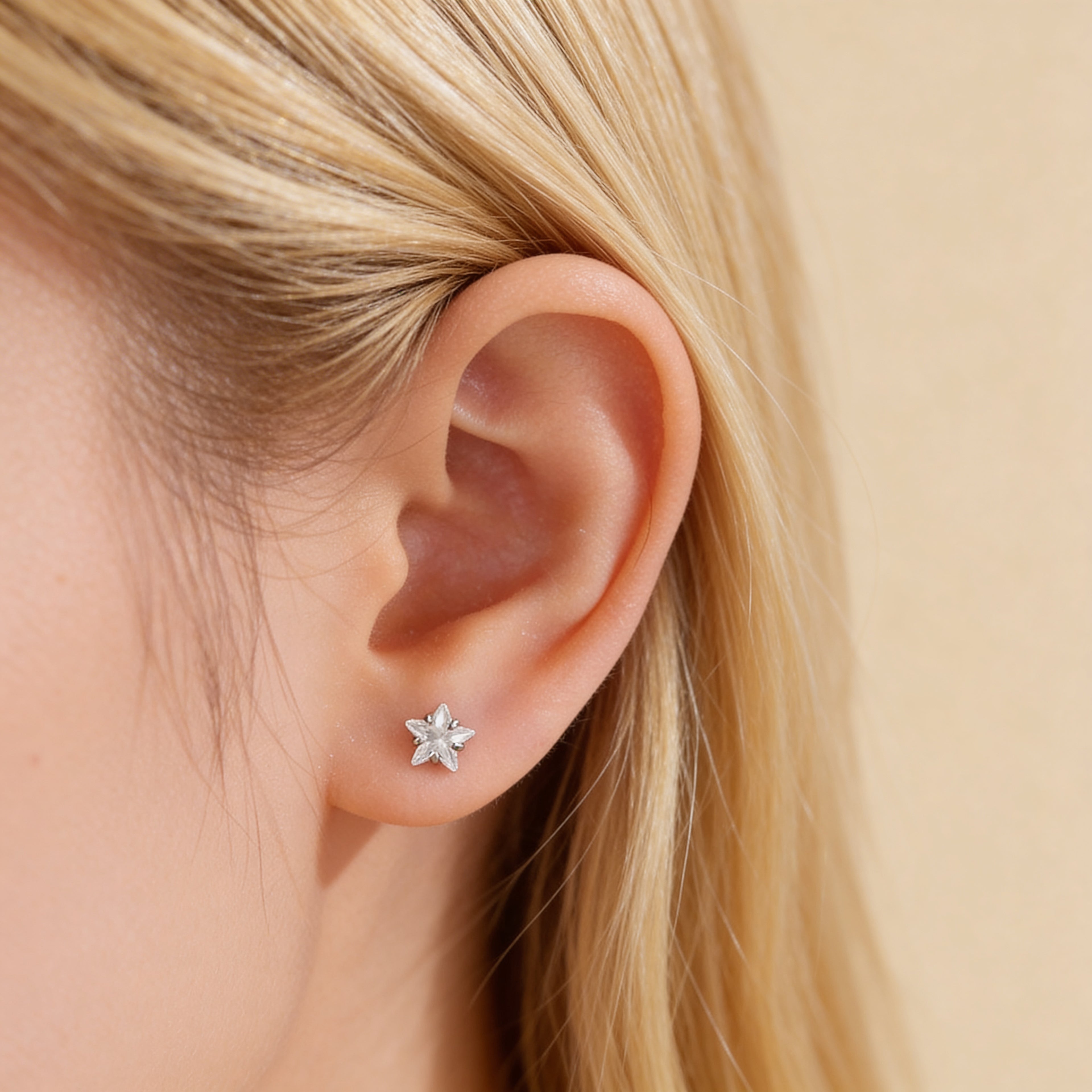 Tiny crystal star stud earrings worn on ear.