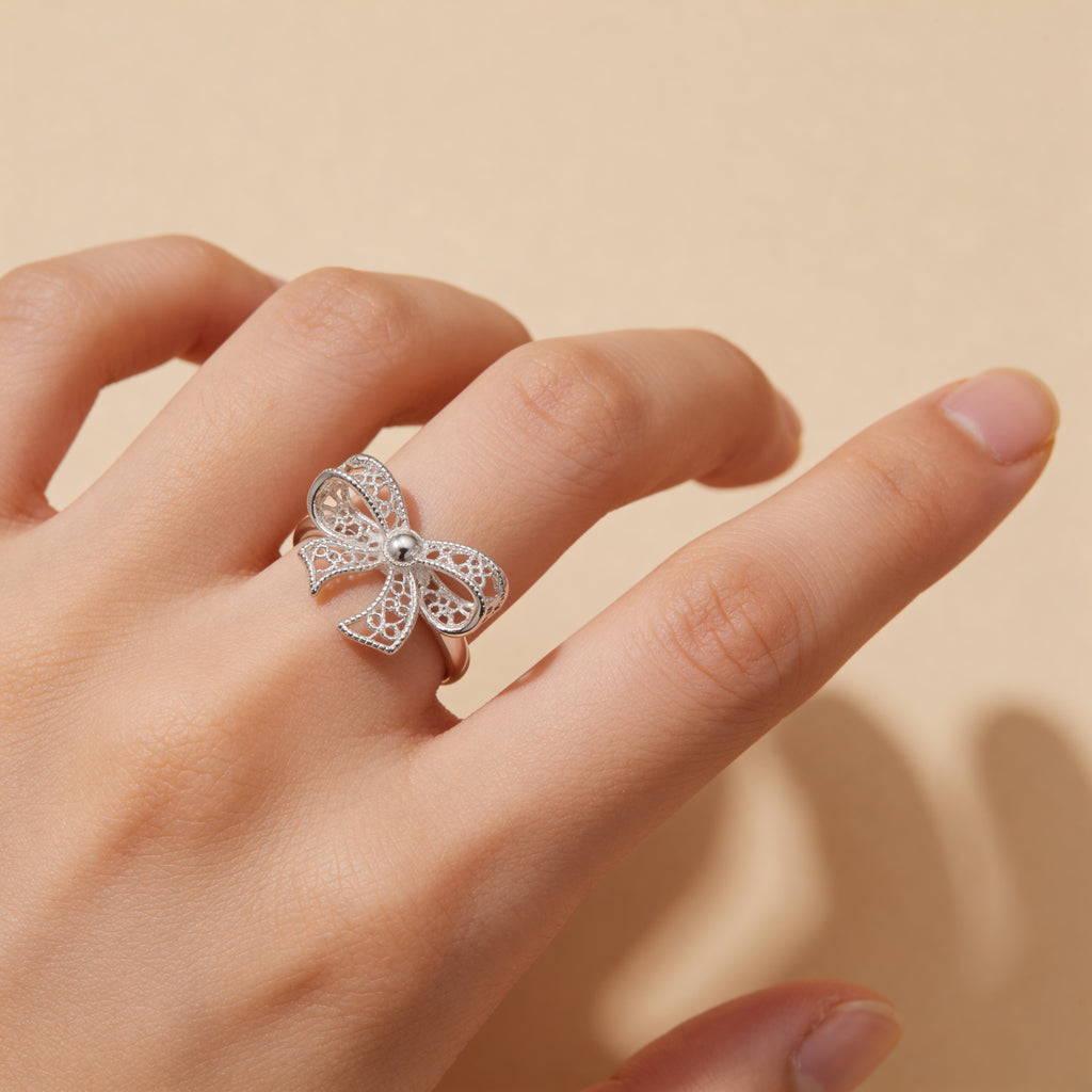Filigree textured bow ring in polished silver plated finish, adjustable design.