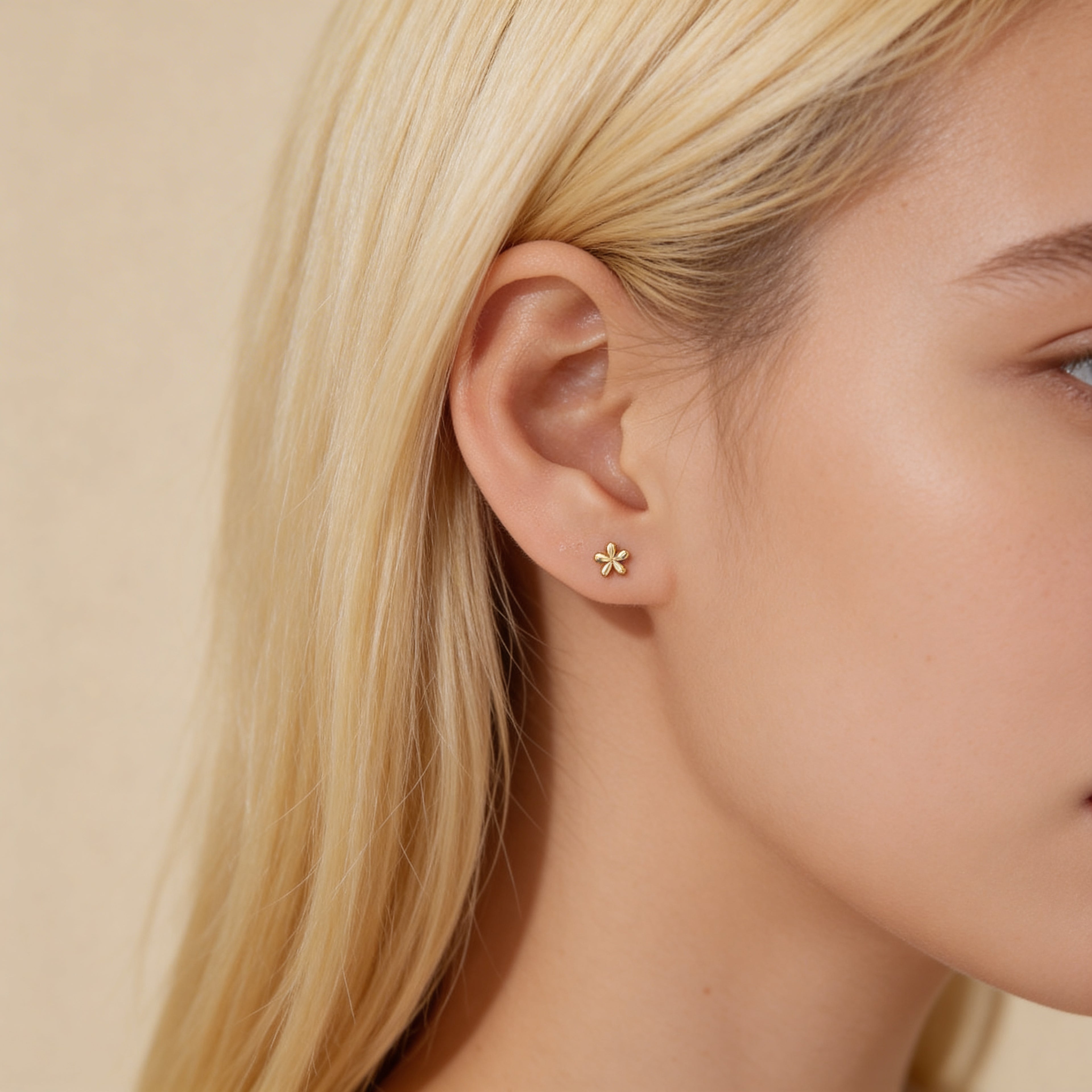 Mini gold flower stud earrings worn on ear.
