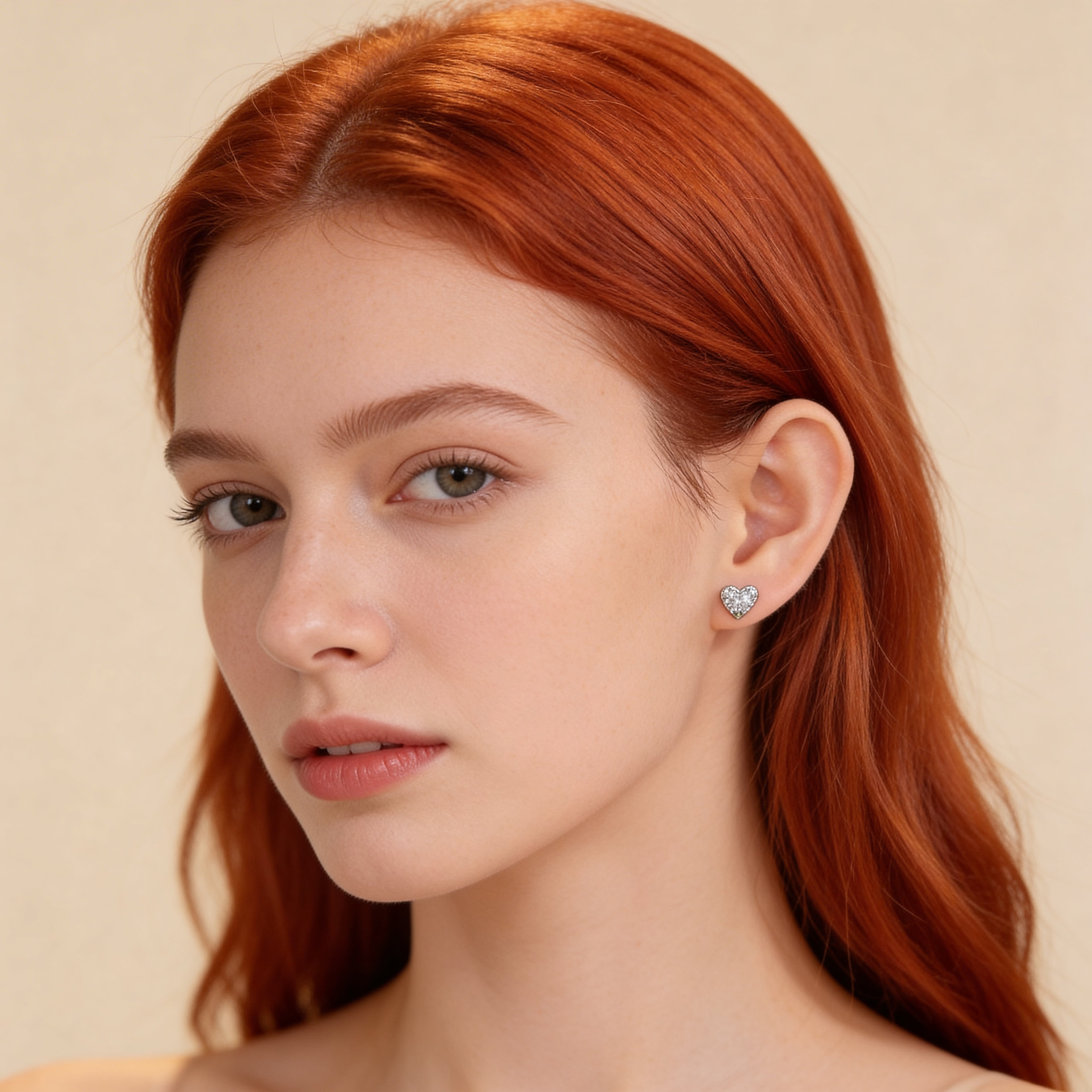 Dainty silver heart stud earrings worn on ear with sparkling stones.