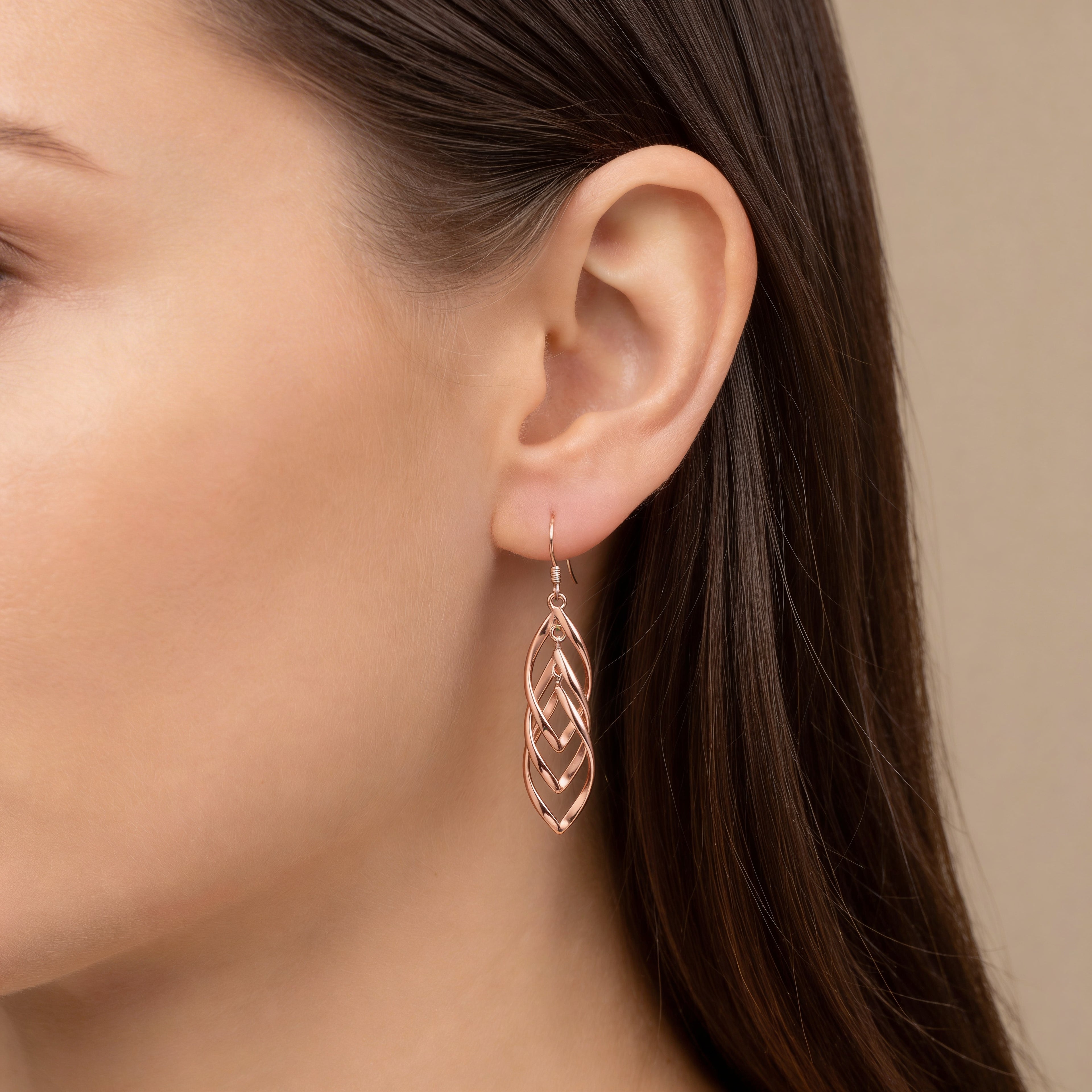 Long rose gold cascading leaf earrings worn on ear.