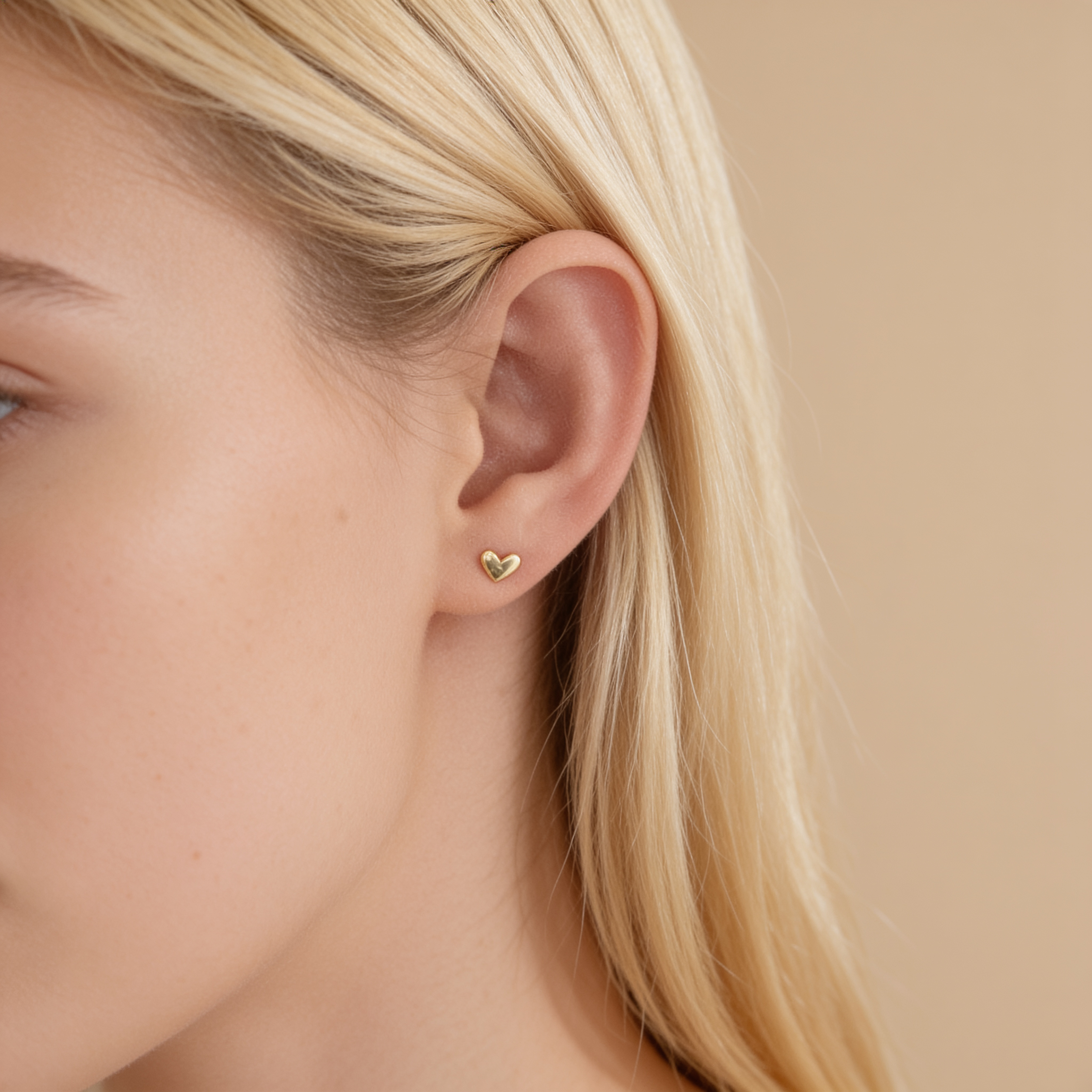 Gold tone mini heart stud earring worn on the ear, showing the delicate 4.8 mm heart design