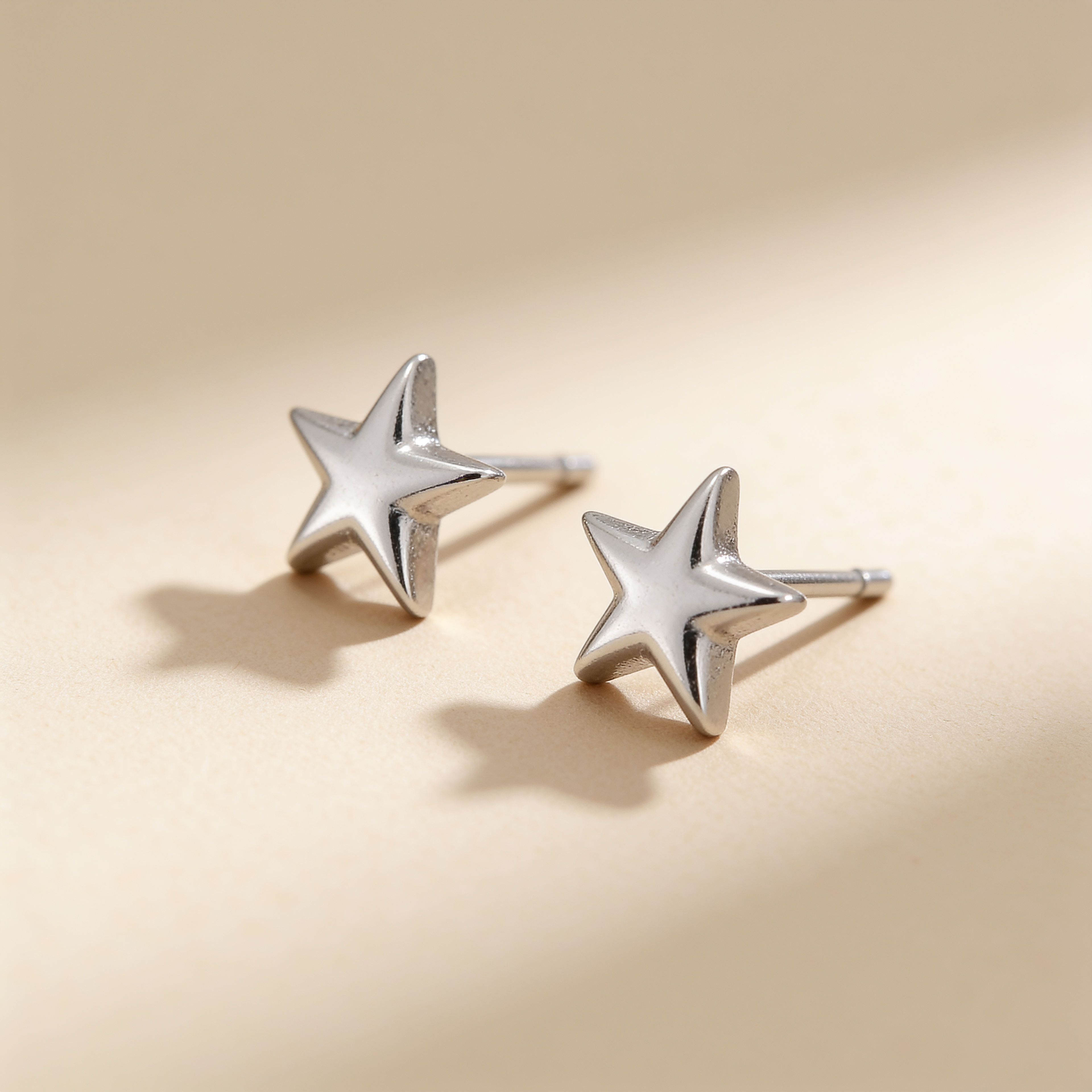 Mini silver plated star stud earrings on a soft beige background