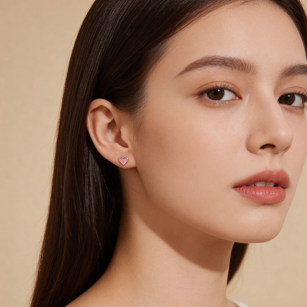 Dainty pink heart stud earrings worn on ear.