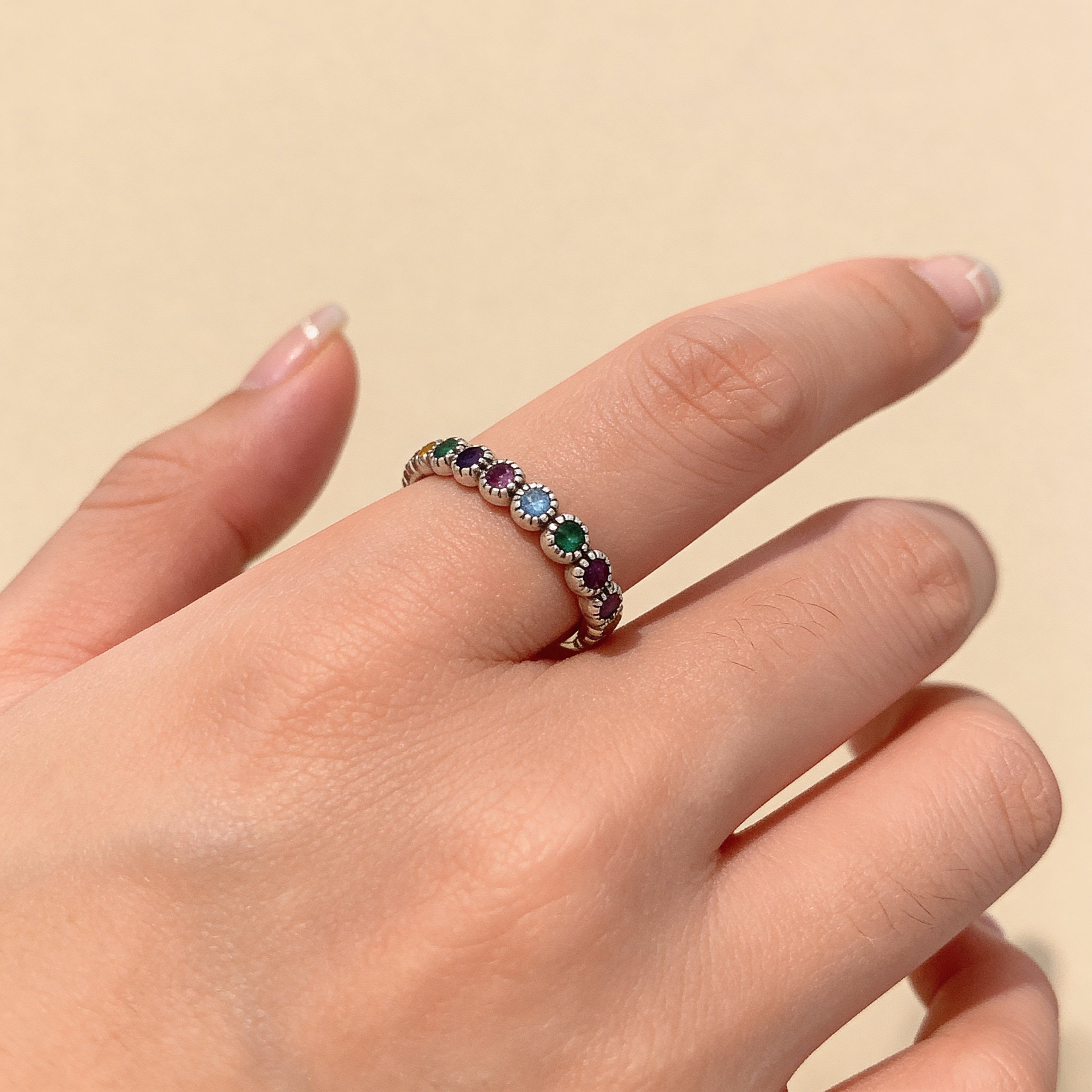 Adjustable silver rainbow stone ring worn on finger, minimalist stacking band for women.