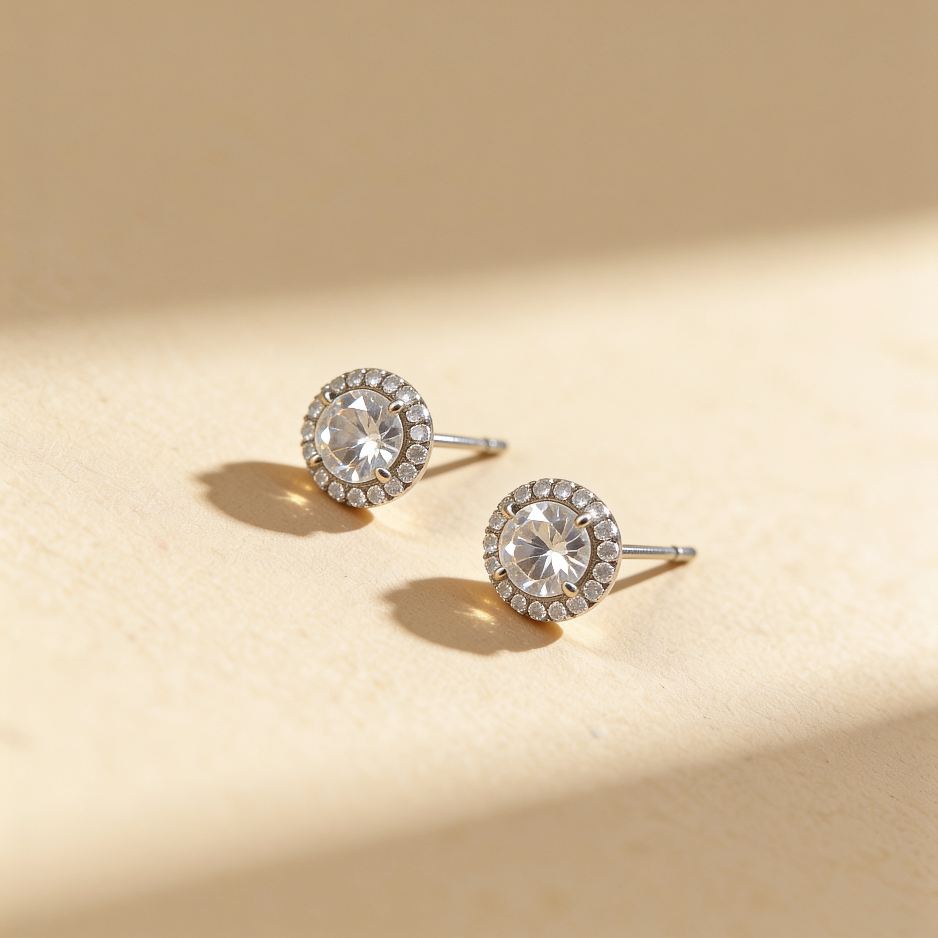 Silver plated round cubic zirconia stud earrings with sparkling crystal halo on a warm beige background
