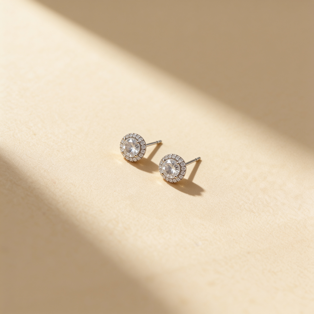 Silver plated round cubic zirconia stud earrings with crystal halo displayed on a warm beige surface