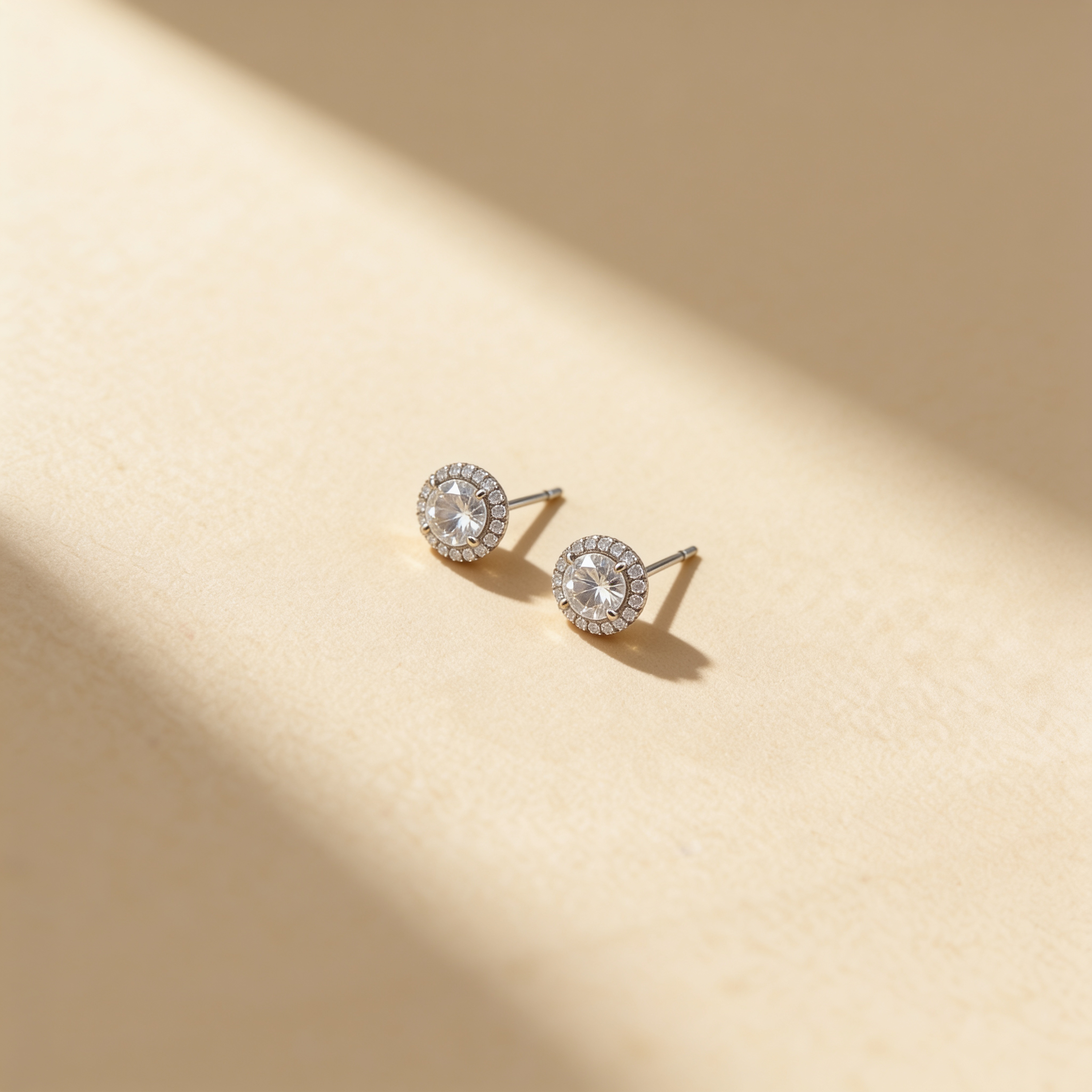 Silver plated round cubic zirconia stud earrings with crystal halo displayed on a warm beige surface