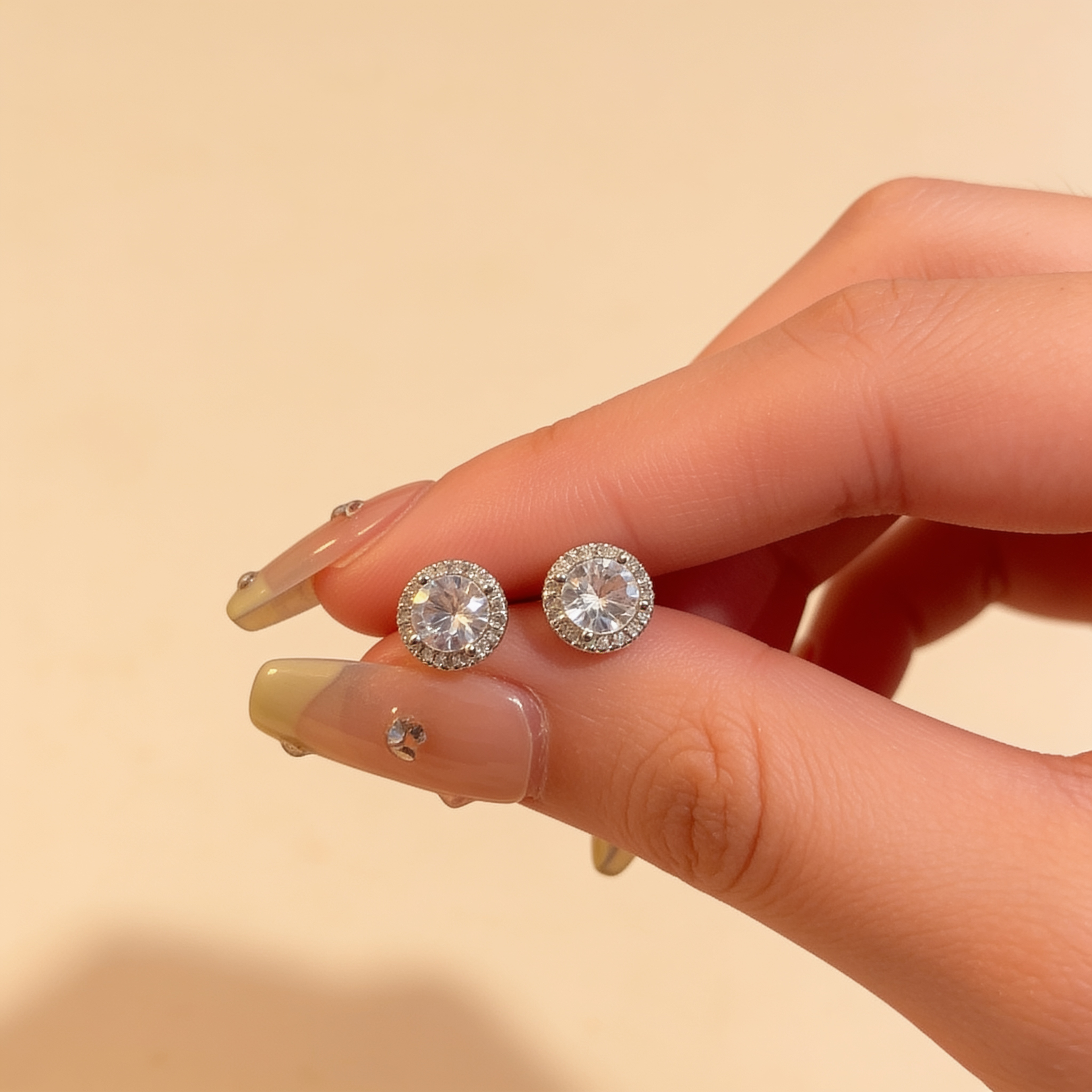 Silver plated round cubic zirconia stud earrings with sparkling crystal halo held between fingers to show their 1.2cm size
