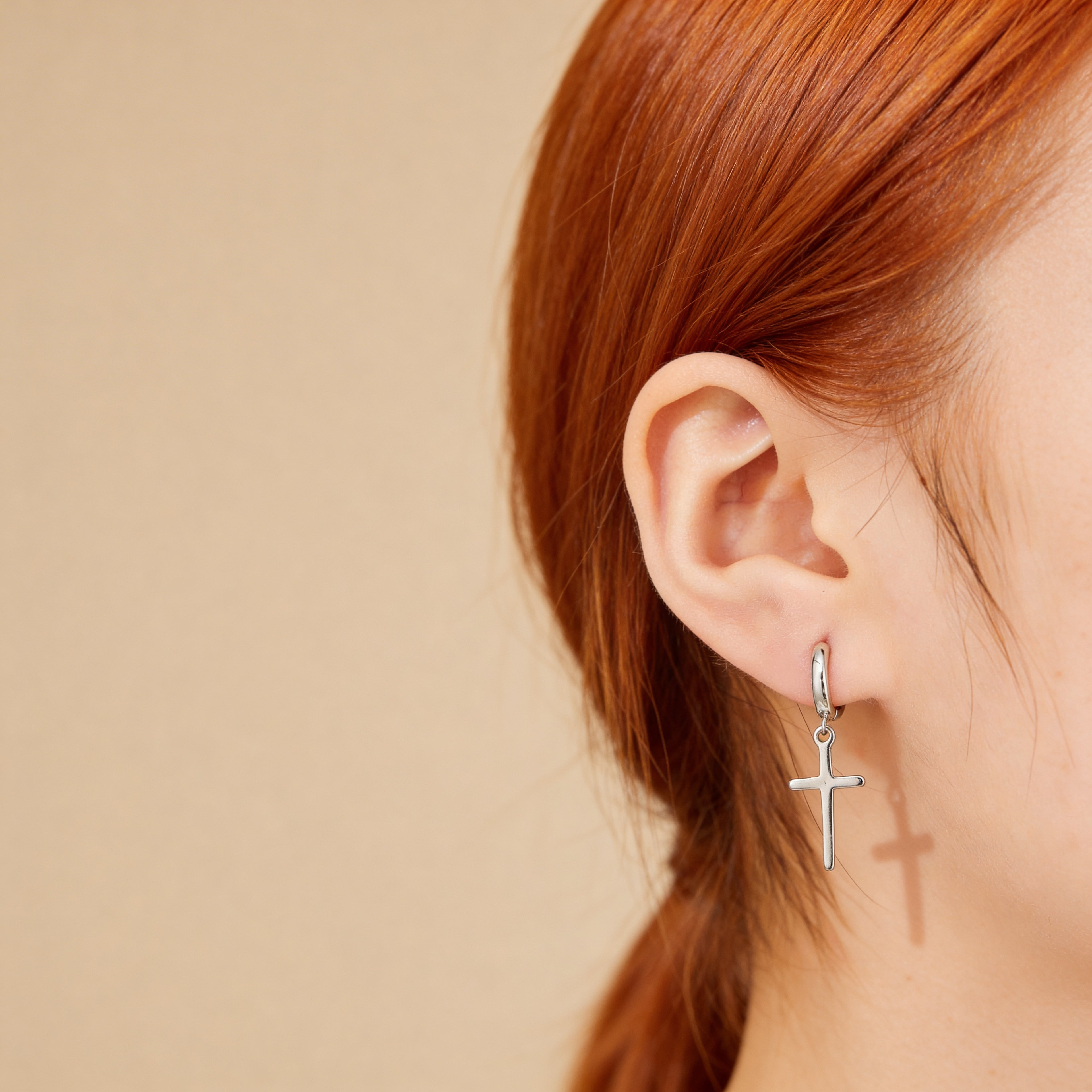 Silver cross hoop earrings worn on ear.