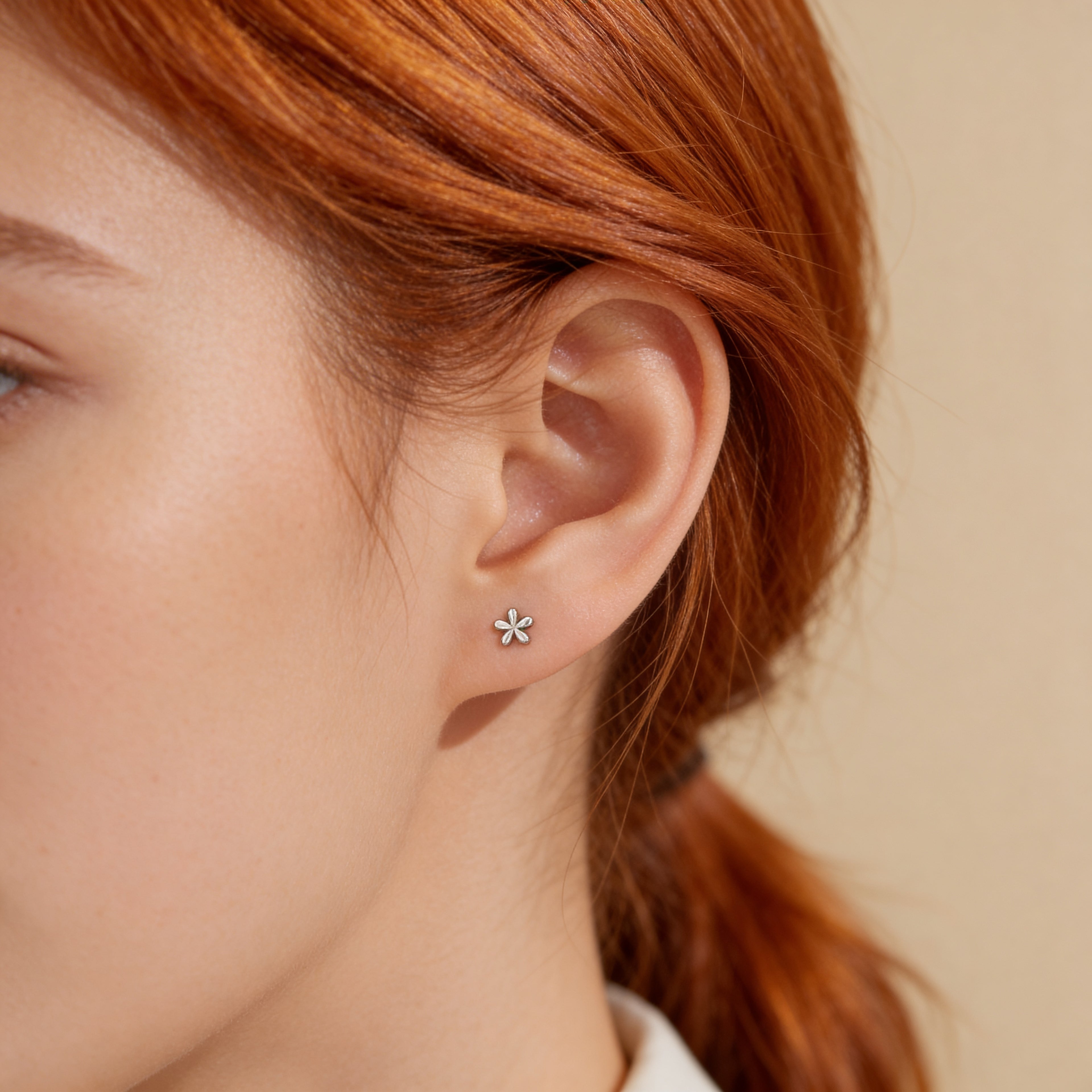 Mini silver flower stud earrings worn on ear.