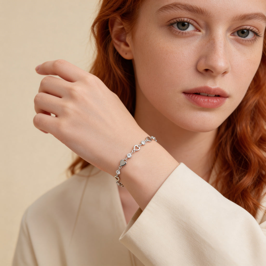 Dainty silver heart link bracelet with CZ stones worn on wrist.