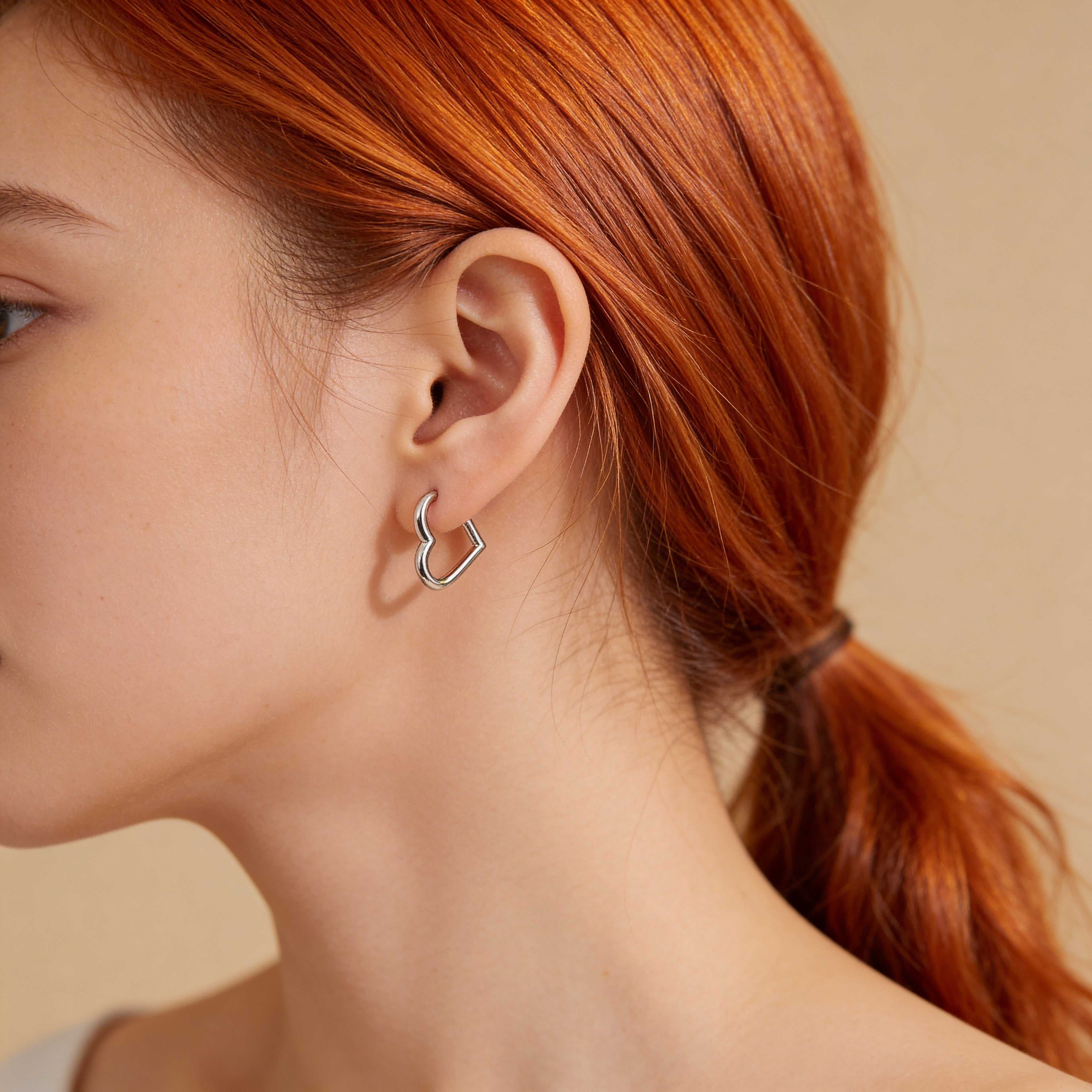 Silver heart hoop earrings worn on ear.