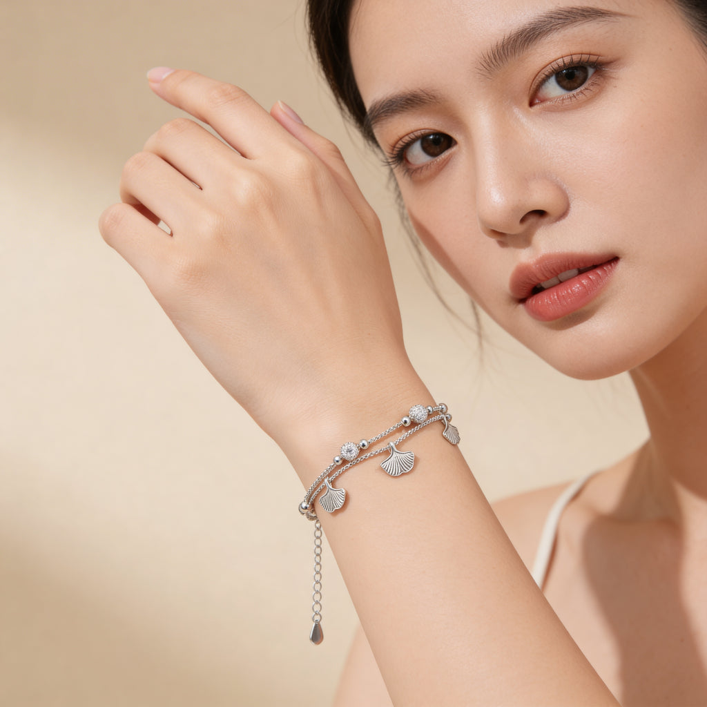 Silver plated leaf charm bracelet worn on wrist.