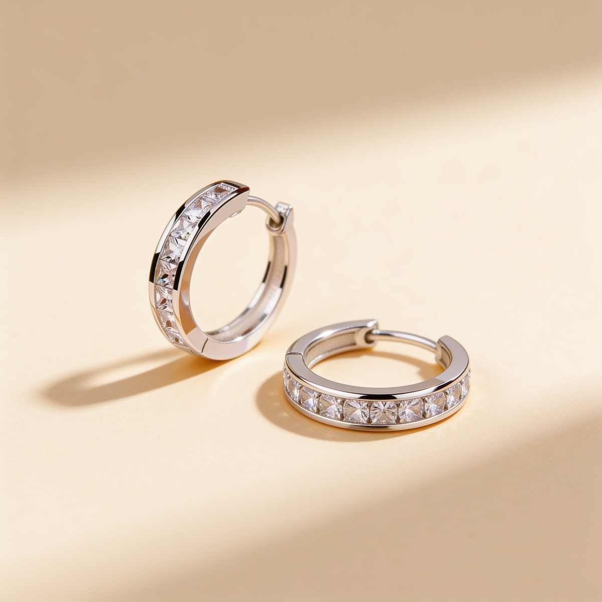 Silver plated crystal huggie hoop earrings with sparkling stones displayed on a warm beige background
