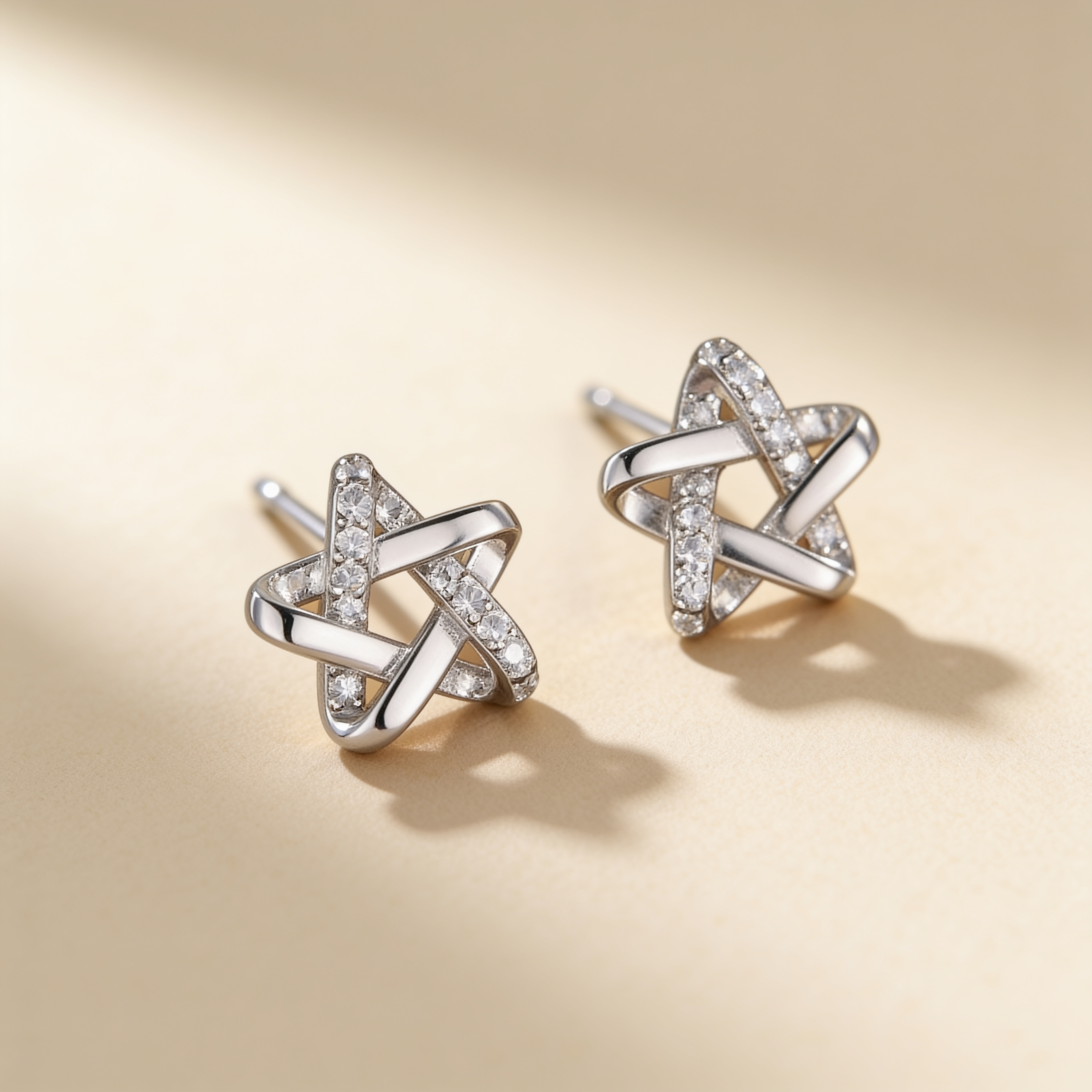 Silver plated star stud earrings with sparkling crystal accents displayed on a warm beige background