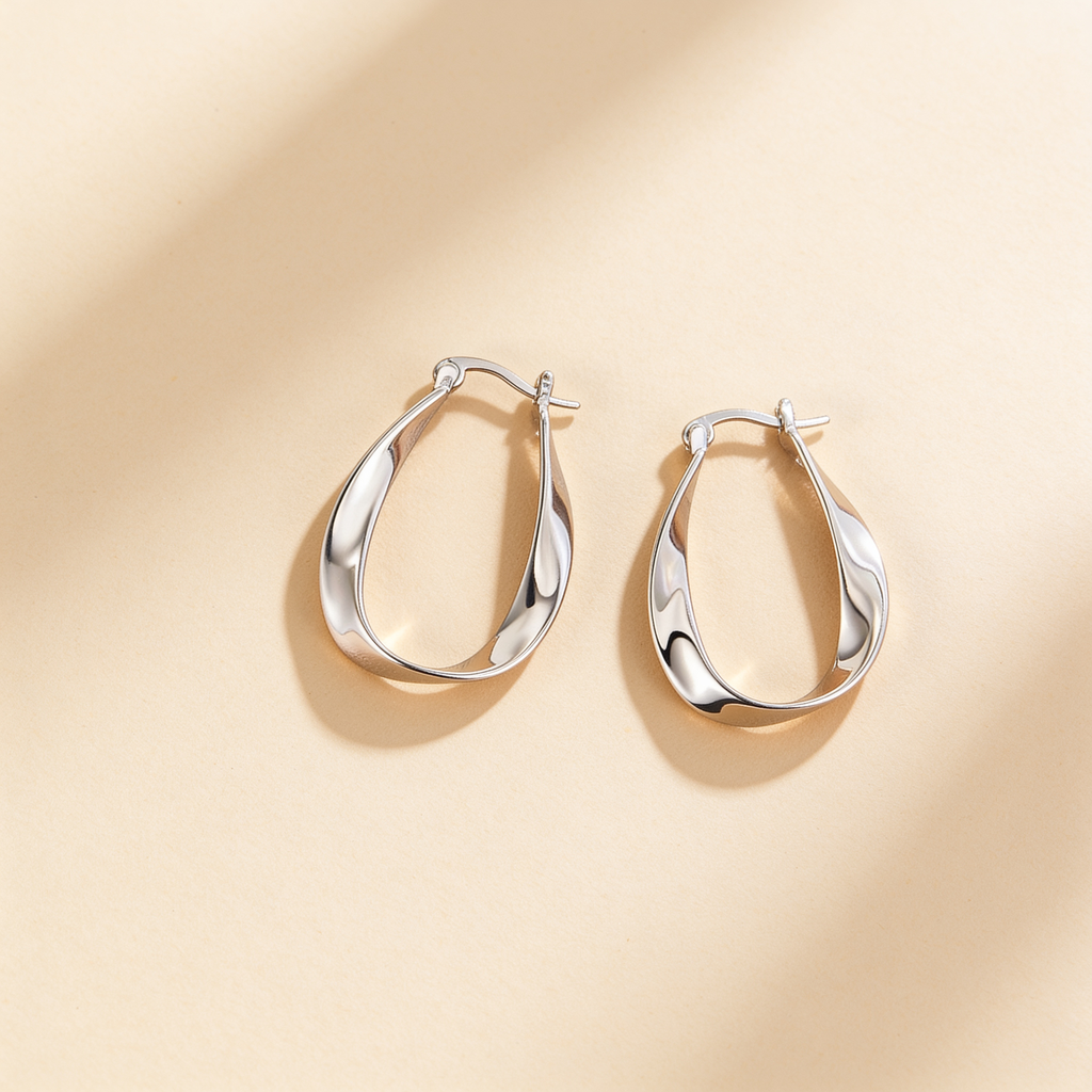 Pair of silver plated twisted hoop earrings with a polished sculpted design displayed on a warm beige background